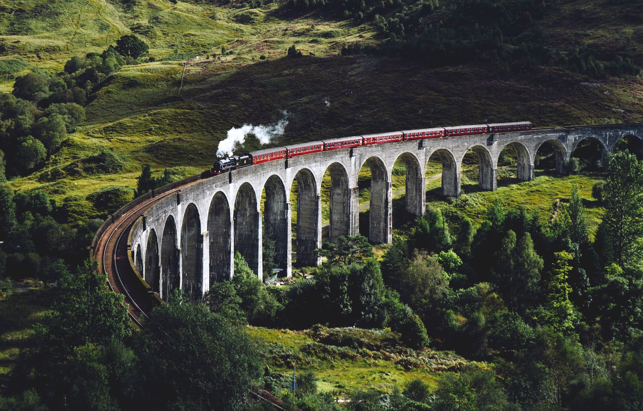 A steam engine train travelling across the Glen Finnan Viaduct in Scotland