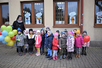 Grupa przedszkolaków z balonikami stoi przed okani biblioteki w Zelowie.