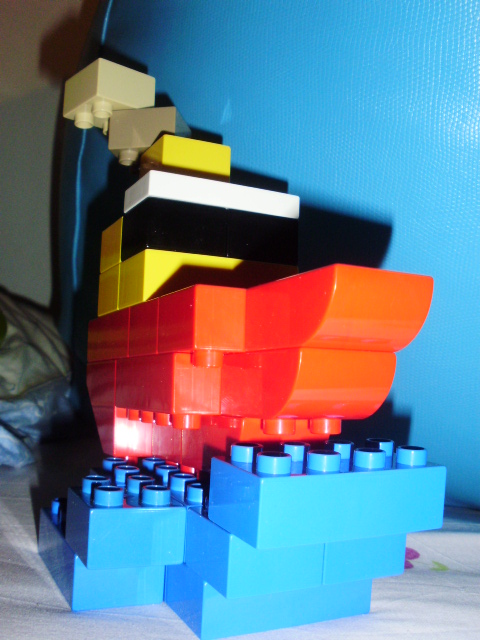 MOC com peças LEGO Duplo, representando um pequeno barco a passar junto a um farol de costa