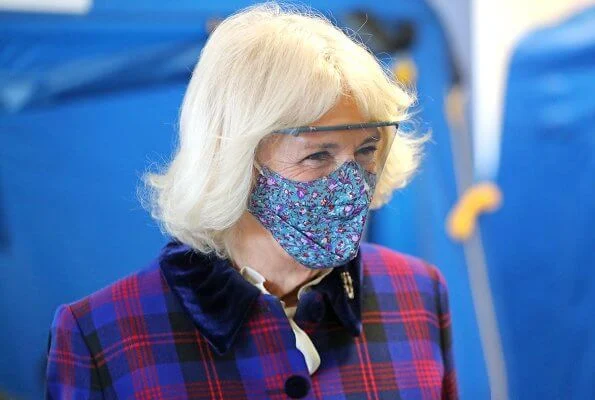 Duchess of Cornwall is wearing a face-mask and protective glasses. The Duchess wore a tartan coat dress, and a printed pattern scarf from Seasalt