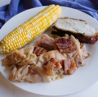A whole head of cabbage wrapped in bacon and braised in beer is a thing of glory. Make it on the grill or in the oven for a flavorful side dish. dinner plate with cabbage, corn on the cob and bacon wrapped pork loin