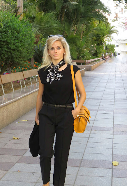 Alejandra Colomera con camiseta negra, pantalón formal negro, lazo en el cuello negro con lunares blancos y complementos mostaza