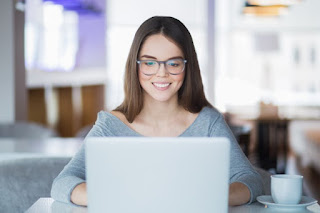 mulher com óculos trabalhando em casa pelo notebook sorrindo