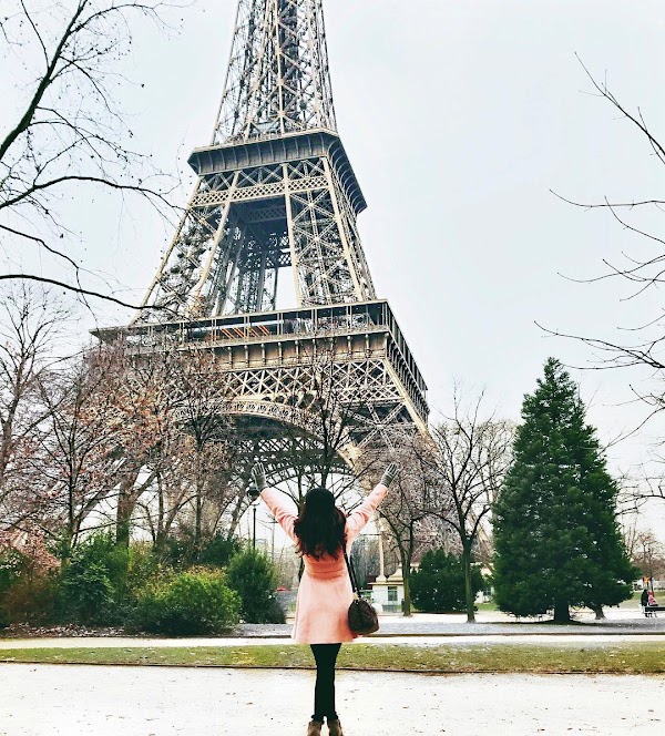 a girl in a pink coat pose in front of the Eiffel Tower