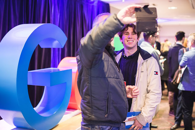 Photo of attendees taking seflies in front of Google signage at event