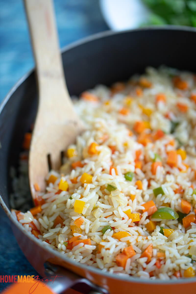 An orange pan of colourful rice with a brown serving spoon