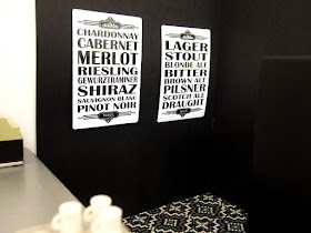 Modern one-twelfth scale miniature bar scene with black and white posters listing drink types on the side wall.