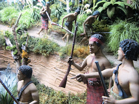 Diorama of 19th-century Maori with muskets on a track in the bush.