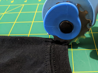 Black fabric laying on green cut board with blue rotary cutter with skip blade cutting holes along the seam