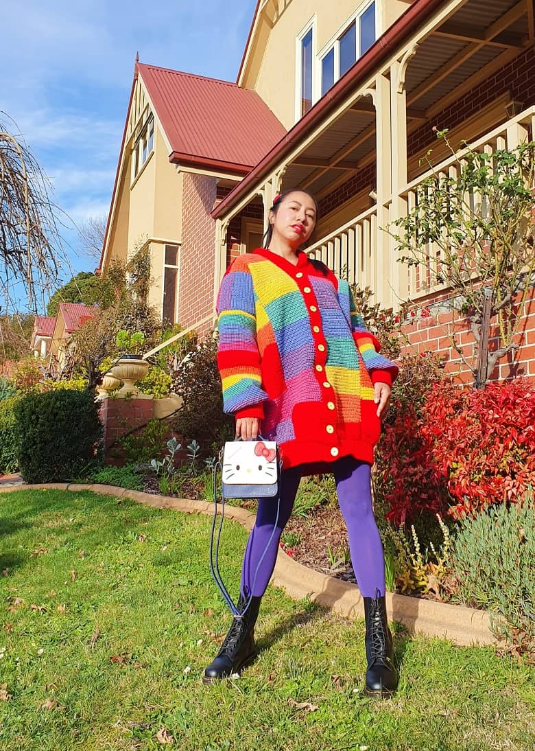 a picture of a girl wearing a crocheted rainbow jumper outdoor