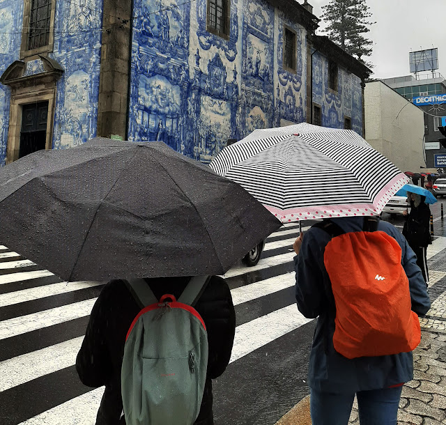 duas pessoas com guarda-chuva a observar uma igreja com azulejos