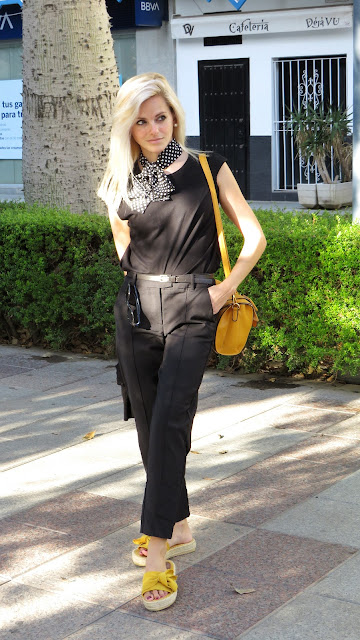Alejandra Colomera con camiseta negra, pantalón formal negro, lazo en el cuello negro con lunares blancos y complementos mostaza