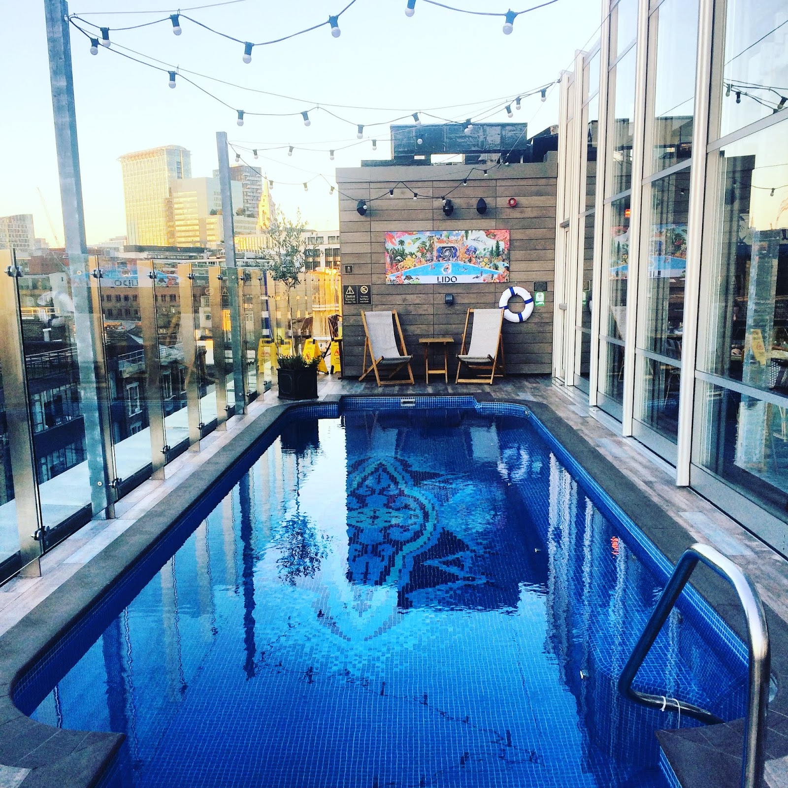 blue swimming pool with deckchairs on roof of london hotel the curtain