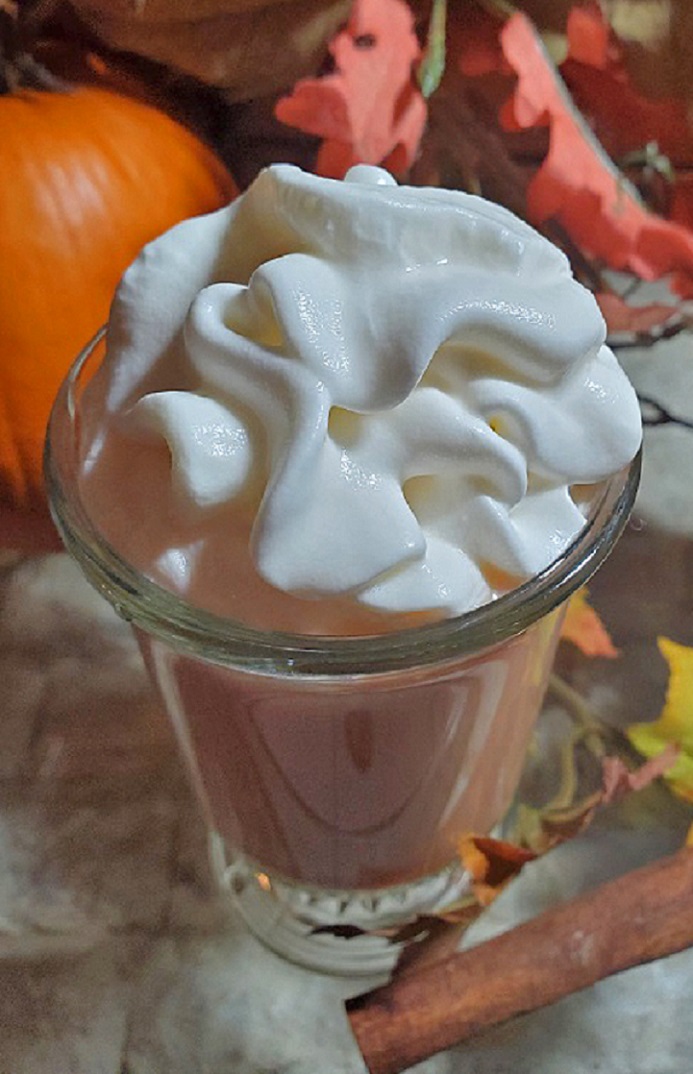 this is a glass cup of pumpkin spice latte coffee with whipped cream and a real pumpkin along with fall leaves and a cinnamon stick