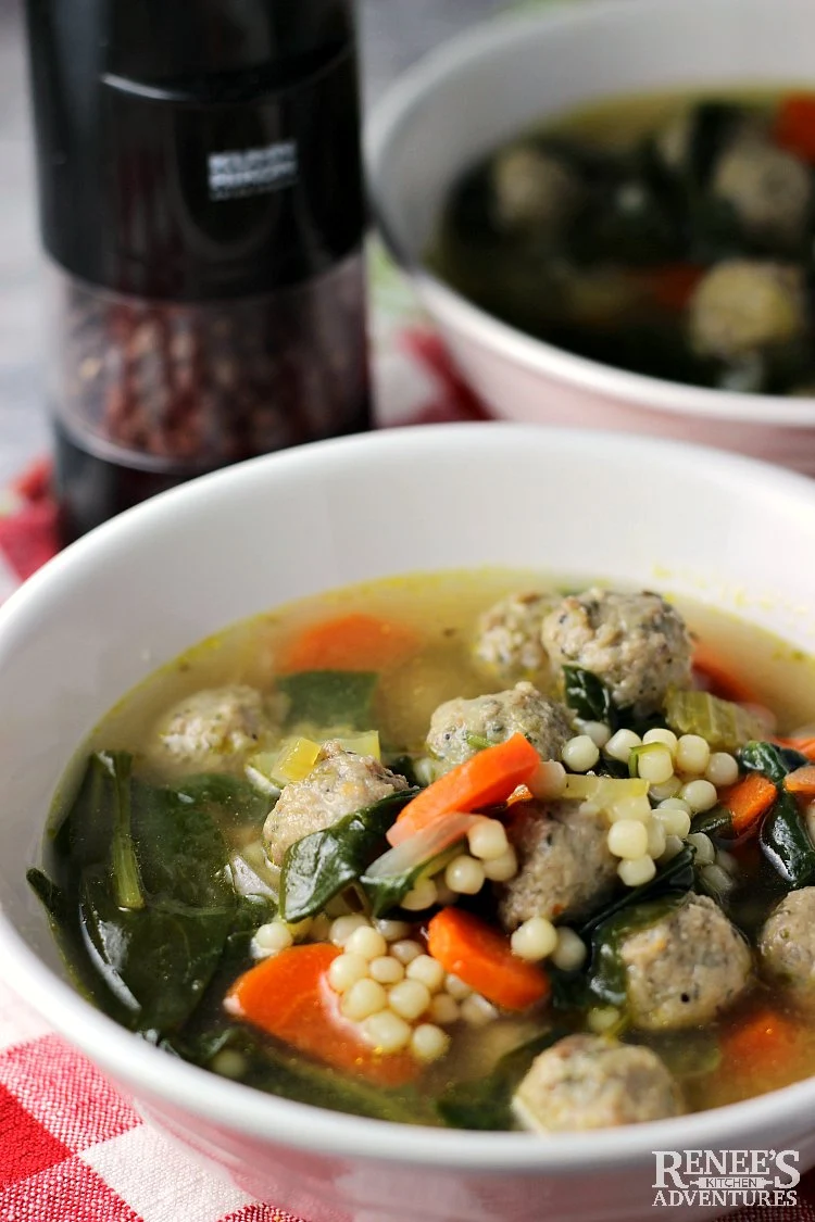 close up view of a bowl of Easy Italian Wedding Soup by Renee's Kitchen Adventures (one in the front and one behind it) with a pepper grinder to the side