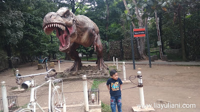 Berfoto di belakang patung Dinosaurus di Taman Lansia