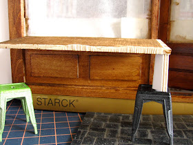 Modern dolls' house miniature cafe, half built, with a mock up of a sloping laneway outside and a large gap between the top of the stools and the table.