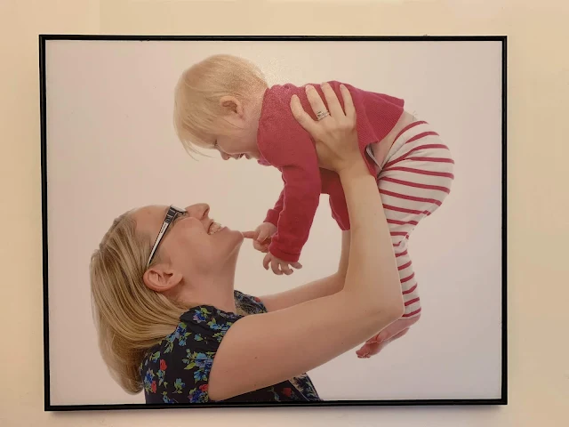 A framed canvas on the wall of a mother holding a small baby in the air