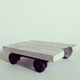 One-twelfth scale industrial-style trolley with rusted wheels and undercarriage and distressed white top planks. 