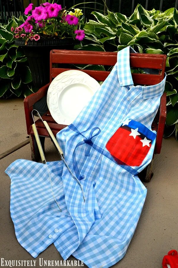 Patriotic Flag Men's Dress Shirt Apron on a red bench with a bbq prong