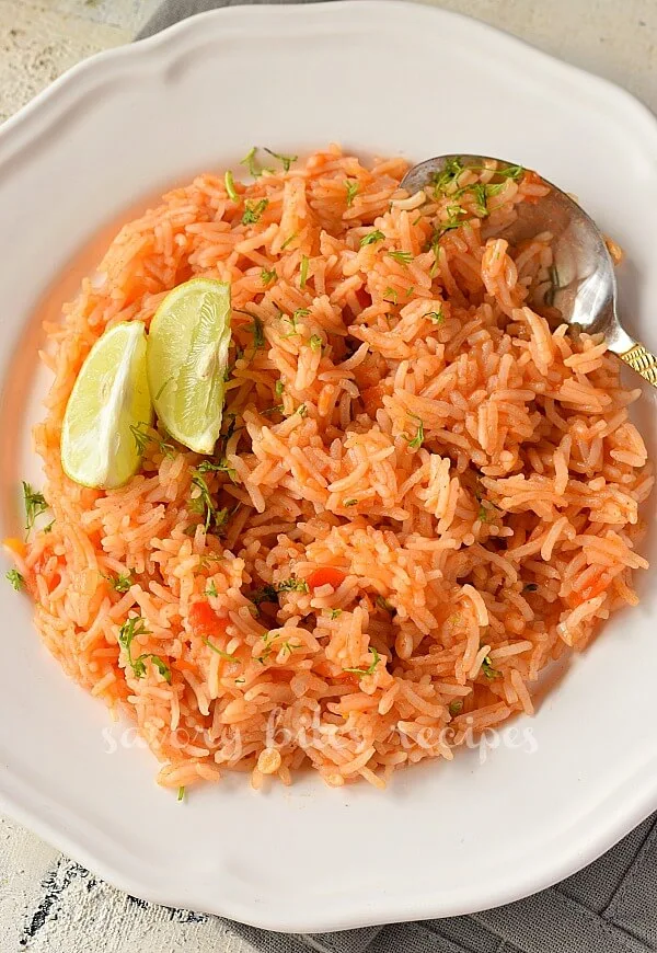 a white plate with best authentic mexican rice topped with cilantro and lime wedges