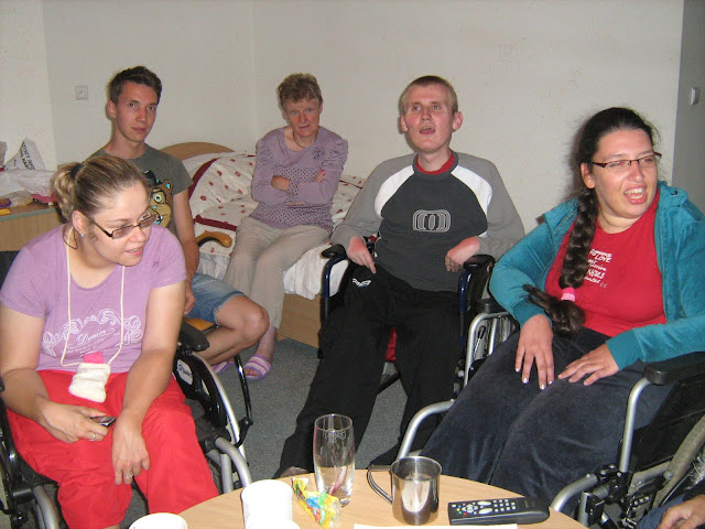 Na zdjęciu widoczne jest wnętrze pokoju hotelowego a w nim uczestnicy turnusu rehabilitacyjno-wypoczynkowego w Szczyrku. Na pierwszym planie widać dwie niepełnosprawne dziewczyny na wózkach inwalidzkich - Olgę i Martę, natomiast na drugim planie na krześle siedzi wolontariusz Paweł oraz dwoje niepełnosprawnych Danka (siedzi na kanapie) i Łukasz (siedzi na wózku inwalidzkim). Wszyscy z zadowoleniem spoglądają w obiektyw aparatu.