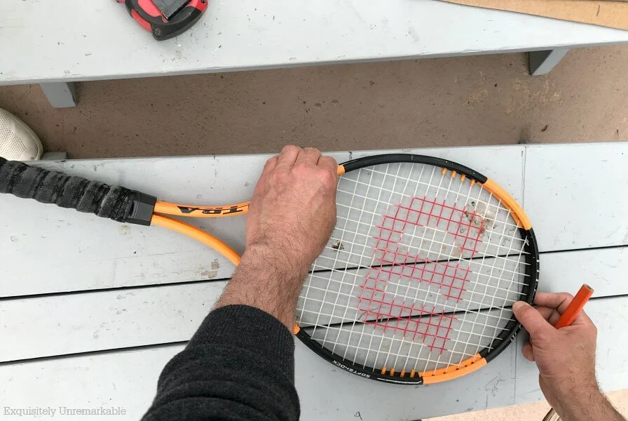Man drawing a curve on a wooden bench with a tennis racket for pattern