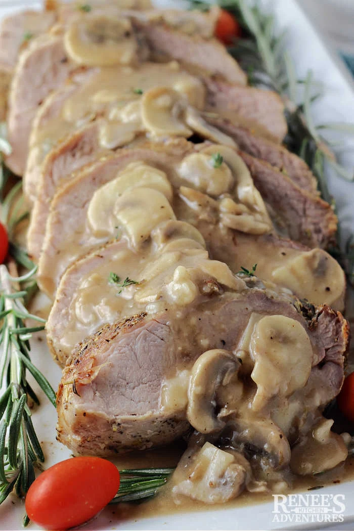 Close up of pork ribeye roast sliced and on platter with mushroom gravy and garnish of fresh rosemary sprigs