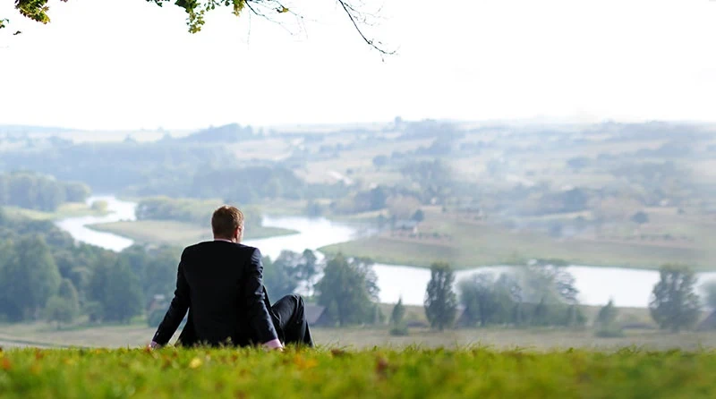 homem sentado na grama contemplando a paisagem à sua frente