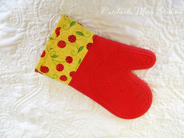 Oven mitt in yellow and red cherry fabric with red silicone.
