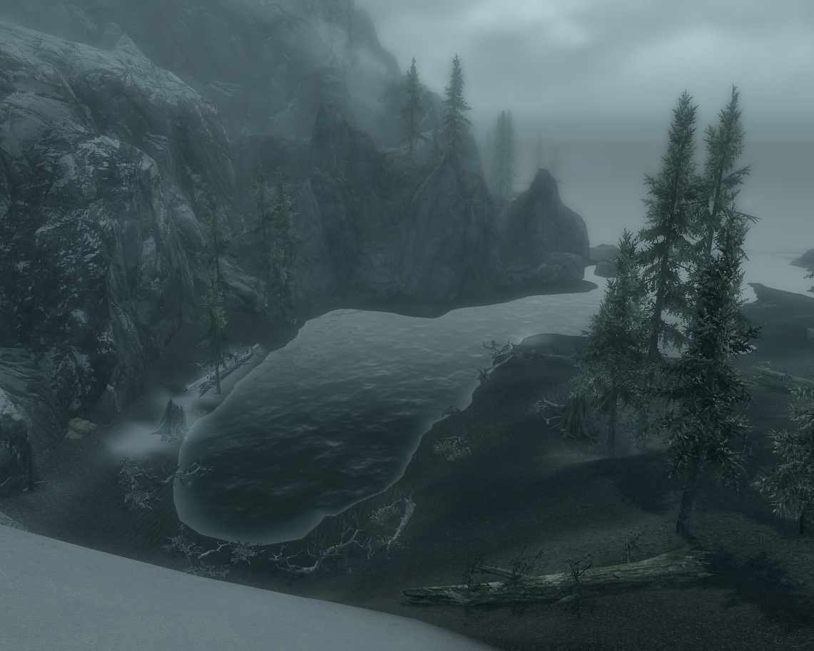 view down a steep snowy slope to a small bay with high mountains on the left and some spruces on the right