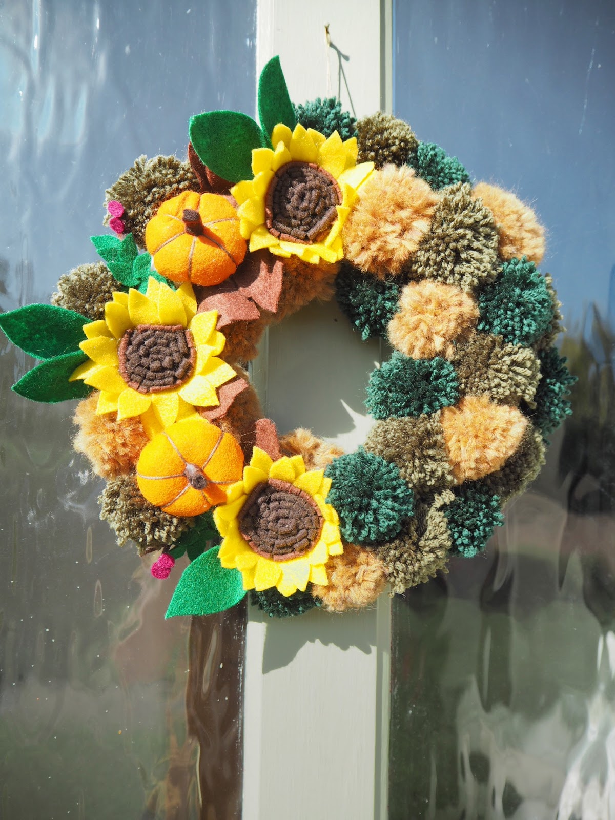 How to make an autumn wreath from felt flowers and woollen yarn pom poms. DIY tutorial for an easy, simple craft you can make yourself. Fall wreath perfect for your front door this season. 