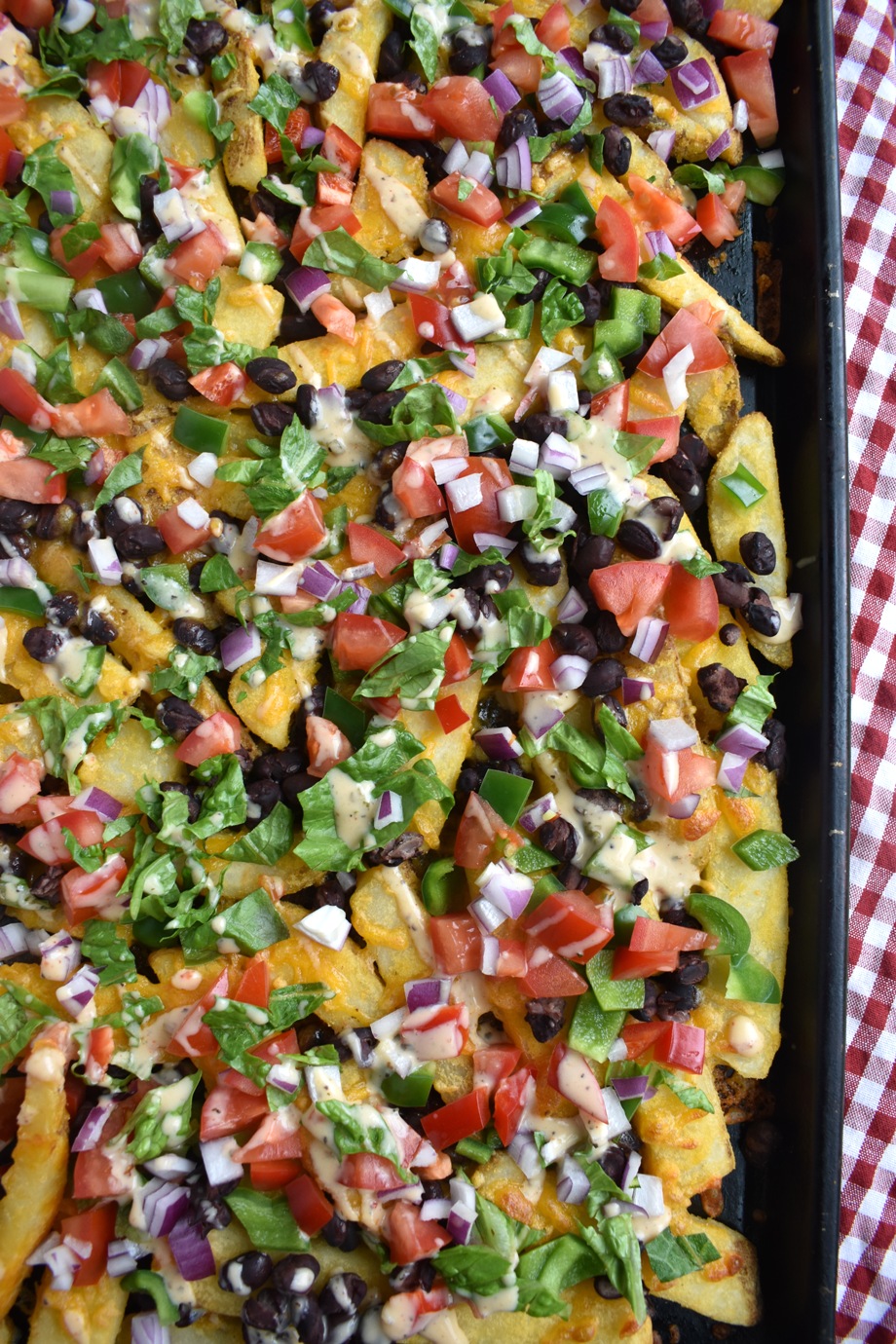 Loaded Nacho Fries feature crispy steak fries topped with melted cheddar cheese, black beans, bell peppers, tomatoes, red onion, lettuce, ranch and salsa for a super delicious and easy appetizer!