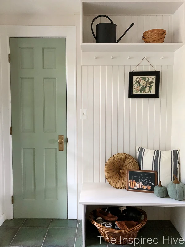 Farmhouse mudroom decorated for fall. Green door, tongue and groove wall, and peg rail hooks. 