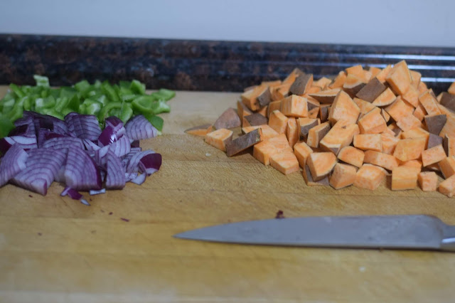 Sweet potato, green pepper, and onion diced on a cutting board. 