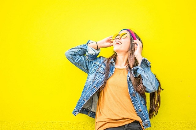 happy woman with sunglasses and pink headband yellow background