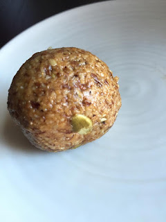 a white plate with a brown, speckled ball made of nut butter, with one visible pumpkin seed.