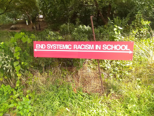 A red sign that says end systemic racism in schools