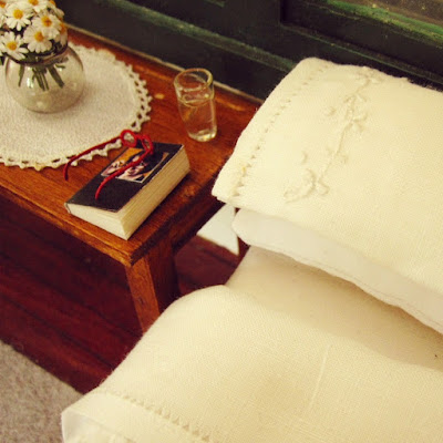 1/12 scale modern miniature bed and bedside table, holding a vase of daisies, a diary and reading glasses and a glass of water.