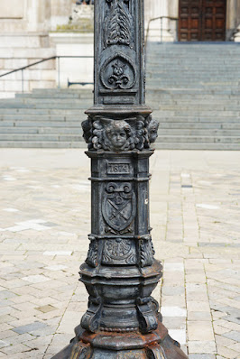 Photograph showing detail on the cast iron lamp post, including the coat of arms and cherubs described in the text.