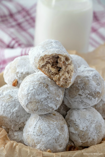 Stacked snowball cookies with a glass of milk with a bite out of the cookie