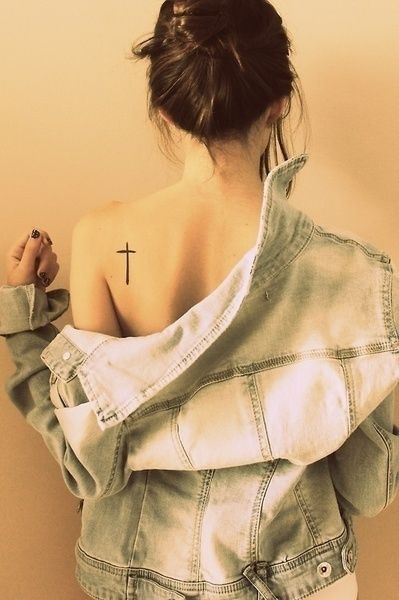 Chica de espaldas usando una chaqueta de mezclilla mostrando su tatuaje en forma de cruz sobre su omóplato derecho