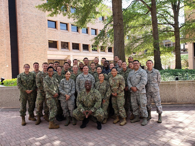 A group of people standing in a brick courtyard in front of a tree.