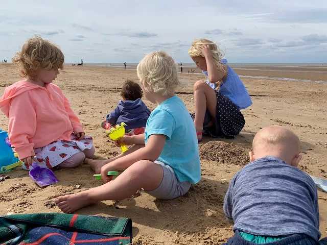 5 children of various ages digging on a sandy beach