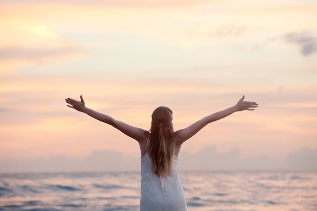Girl with arms wide open in front of sea and sunset.