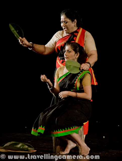 Here are some more pictures from the play Chandalika. To give you some context of the play, it was written by the legendary Rabindranath Tagore and it is the tale of Prakriti, an untouchable girl forced to live on the periphery of society as ‘chandalika’. No one want to play with her, people keep distance from her but at times interact with her for their personal benefits. The play is based on a story from a Buddhist text. Play starts with some dialogs by Usha Ganguli where she describes the situation of her region without water and how people are crying for water. Usha is playing main role in this play. She has a daughter and both of them are treated badly by higher society. At the same time, she helps the local kingdom by helping in various problems like water scarcity. Setting and expressions are two powerful tools used to assist dialogs and action in drama for conveying important information to the viewers. Through these tools a lot can be shown without actually being said. For example, firewood, earthen pots etc. show a rural setting and may also indicate that the play is set in past. Everything cannot be expressed in words because then  the play will be much too lengthy, boring and unintelligent.Interactions between characters, their expressions and their actions often hide a subtext that is very interesting to unearth. For example, in this scene, can you make out what the character is feeling of thinking without actually knowing what is going on? One can easily assume that the character is not unhappy and may even be pleased about things. I can also see a hint of dreaminess in the eyes and may be lost in thoughts about her beloved. But then that is my interpretation and how close it is to the actual emotions being portrayed by the character depends upon the character's acting skills and my ability to read expressions. The expressions here are more of defiance and questioning. But then again that is my interpretation and I can be wrong. Another thing you'd want to note is the attire and the make-up. All efforts are made to keep them true to the situation, the period, and the story. For example, here the dhotis and the lathis indicate that the setting is rural and the expressions of various characters indicate their emotions. For example, the person who is chained is reluctant to go where he is being led and the person in the red dhoti seems to be pleased with himself and takes pleasure in the predicament the chained person is in. Flowers, dances, audience, claps indicate celebrations of either a festival or an event. Some people are wearing garlands and this may indicate their special place in the society. Graceful dance moves and melodious singing are all often a part of dramas and I am amazed by the number of talents most of the stage artists hide within themselves. Almost all of them sing well and dance well along with obviously acting well. One-on-one interactions are some of the most interesting interactions in a play. They reveal more about a character and her relationships with other characters than any other interaction in a play. These are usually more difficult to carry out because the audience is focussed upon the characters involved. These are more challenging for the actors than for the directors.Multiple characters interactions are more challenging for the playwriter and for the director because it requires exceptional skills to craft such scenes. Colors and body languages tell stories of themselves. The next time you go to watch a play, try to keep an eye on these things and you will be amazed at what you will discover.Presence of objects such as cages can be symbolism that you had never suspected. If you observe these things, you will add layers to your play-watching experience. For example, here it is clear that the woman in the centre is someone who has power over the other two. The cage represents imprisonment or curtailment of freedom. The attire of this woman indicates affluence and her demeaner indicates power and even royalty. Is there anything else you can make out? Feel free to leave a comment if you can. The body language of the characters here indicates a mother-daughter relationship. And the leaves and the leaves indicate some sort of a ritual or religious practice. The clothes of these two characters are much simpler. The characters are not affluent but aren't poor either. Let me know if you can read more into these pictures. I would love to know. Please feel free to leave a comment.
