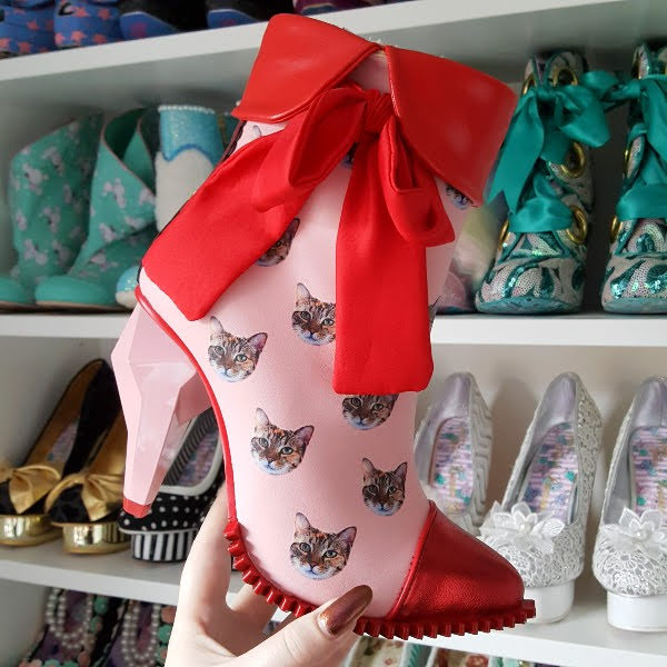 holding pink cat ankle boot with diamond heel in front of shoe shelves