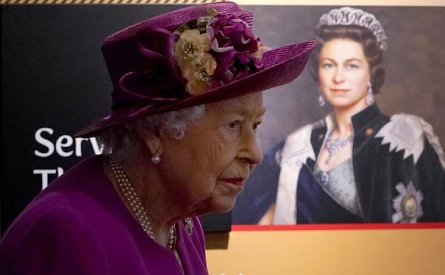 The Queen wore a floral print dress and purple coat and purple hat. diamond brooch