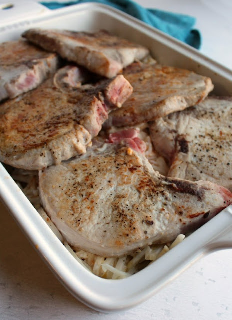 Pork chops, cheesy potatoes and a crunchy topping are baked together to make one absolutely delicious family friendly meal. All you need is a vegetable and dinner is done! browned pork chops over potatoes in casserole dish ready to bake