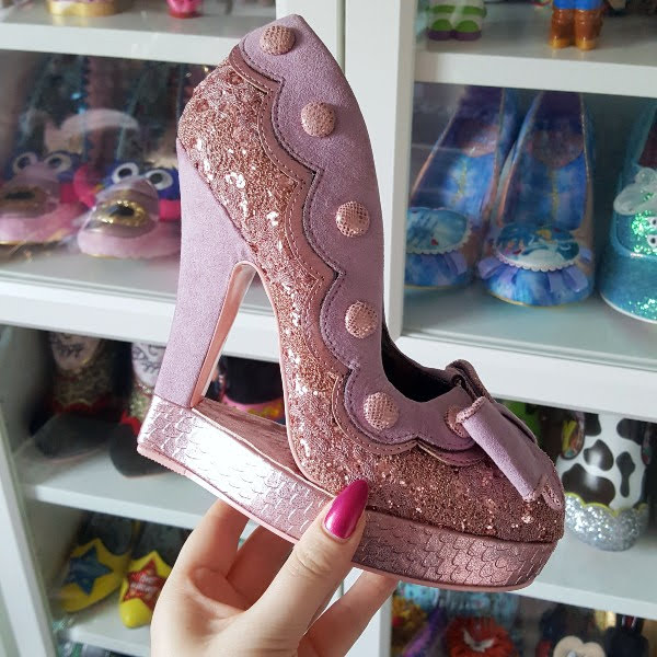 Irregular Choice Queenie pink lace and suede shoe held in hand with shoe shelves in background
